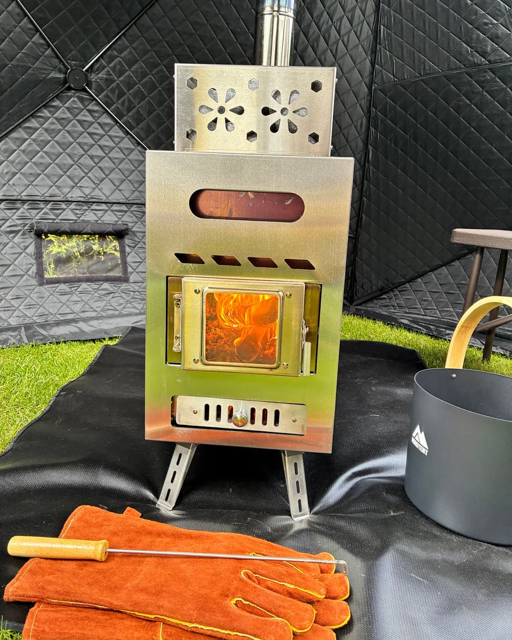 Den vedeldade kaminen brinner inne i bastutältet, med bastustenar, handskar och hink bredvid